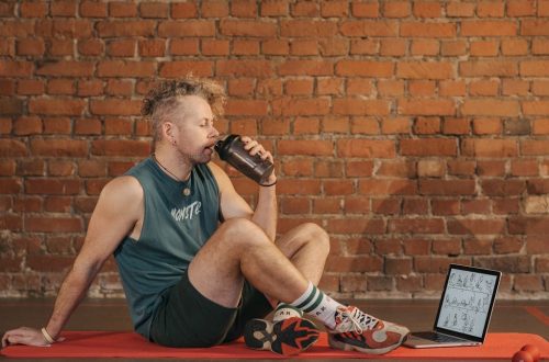 Athletic man sitting on exercise mat with water bottle, taking a break from workout, in a rustic indoor setting.