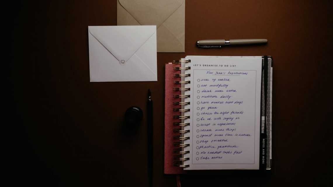 Overhead view of a to-do list notebook with New Year's resolutions, pens, and envelopes on a desk.